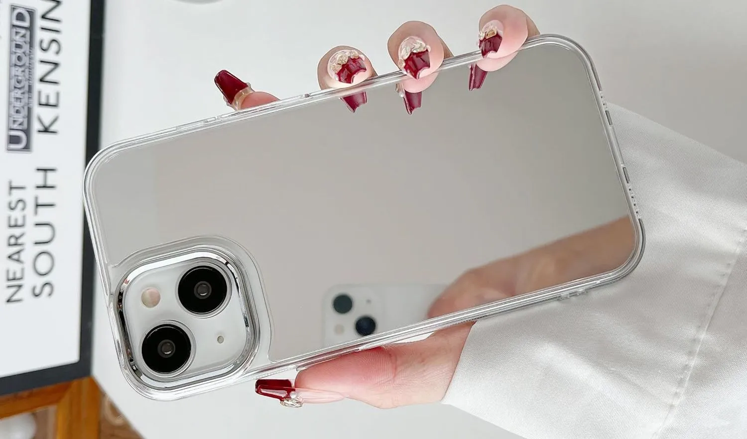 Bàn tay đang cầm một chiếc iPhone được trang bị ốp lưng tráng gương, biến mặt lưng thành một chiếc gương tiện lợi.