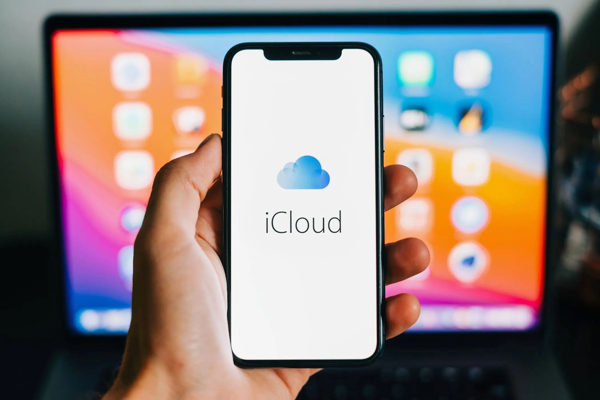 Biểu tượng iCloud hiển thị trên màn hình iPhone, phía sau là MacBook, thể hiện sự tích hợp hệ sinh thái Apple