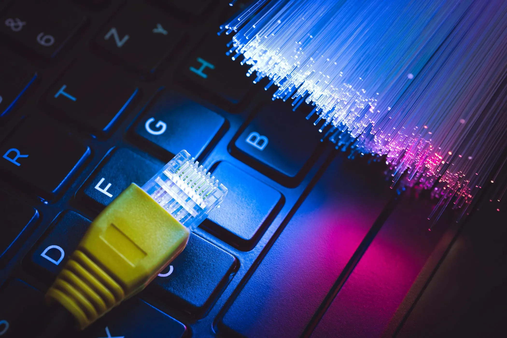 Cáp Ethernet kết nối với bàn phím laptop cùng cáp quang, tượng trưng cho kết nối internet tốc độ cao và băng thông rộng cần thiết cho trải nghiệm mạng ổn định.