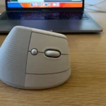 Chuột không dây Logitech Lift màu đen đặt gần laptop trên bàn làm việc