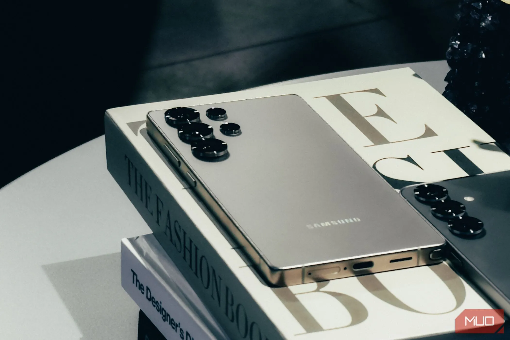 Điện thoại Samsung Galaxy S25 màu bạc Silver Shadow đặt nghiêng trên một cuốn sách, làm nổi bật thiết kế kim loại cao cấp và độ mỏng của thiết bị.