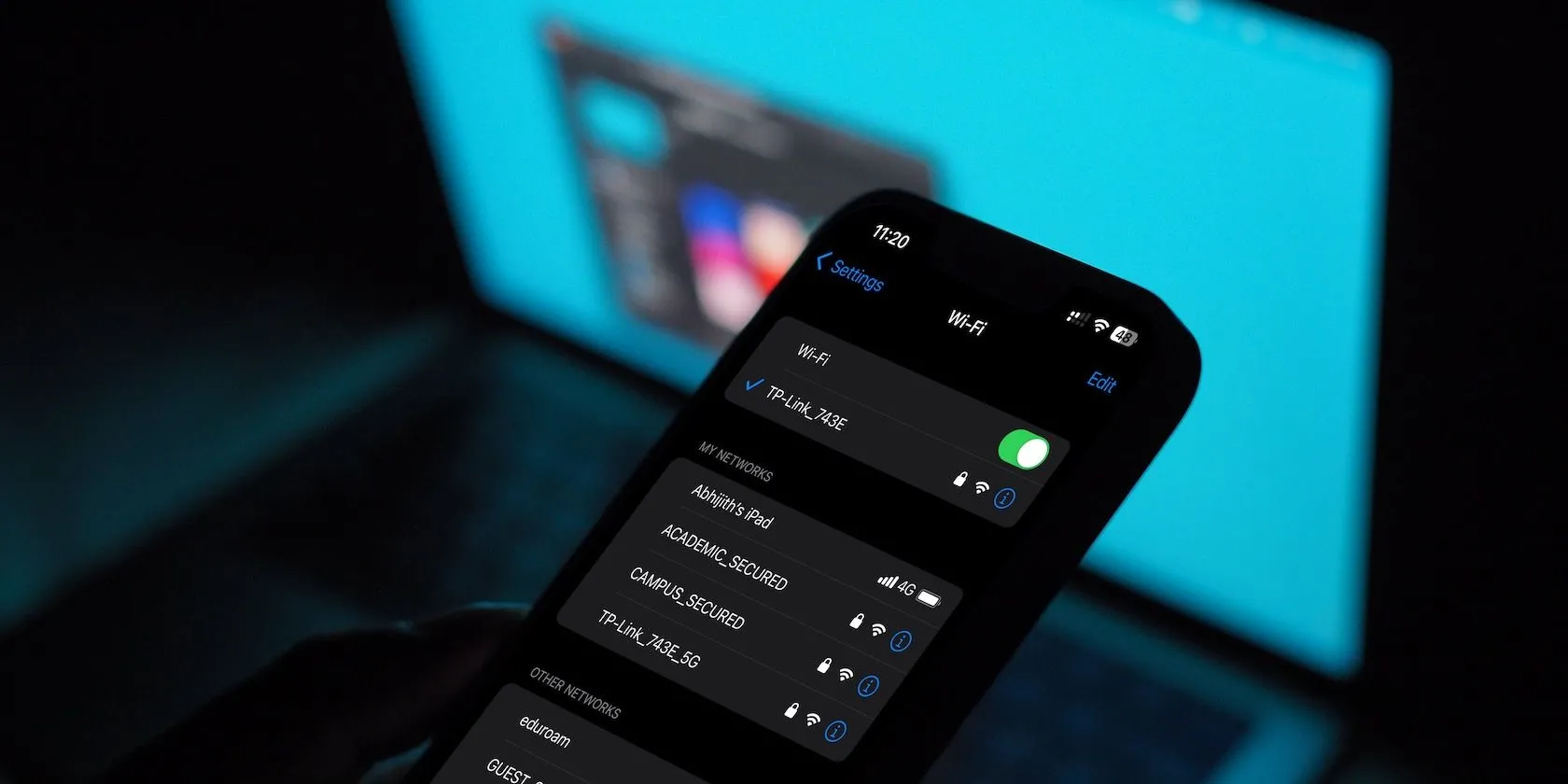 Giao diện cài đặt Wi-Fi trên iPhone với máy tính MacBook ở nền, minh họa việc quản lý kết nối Wi-Fi