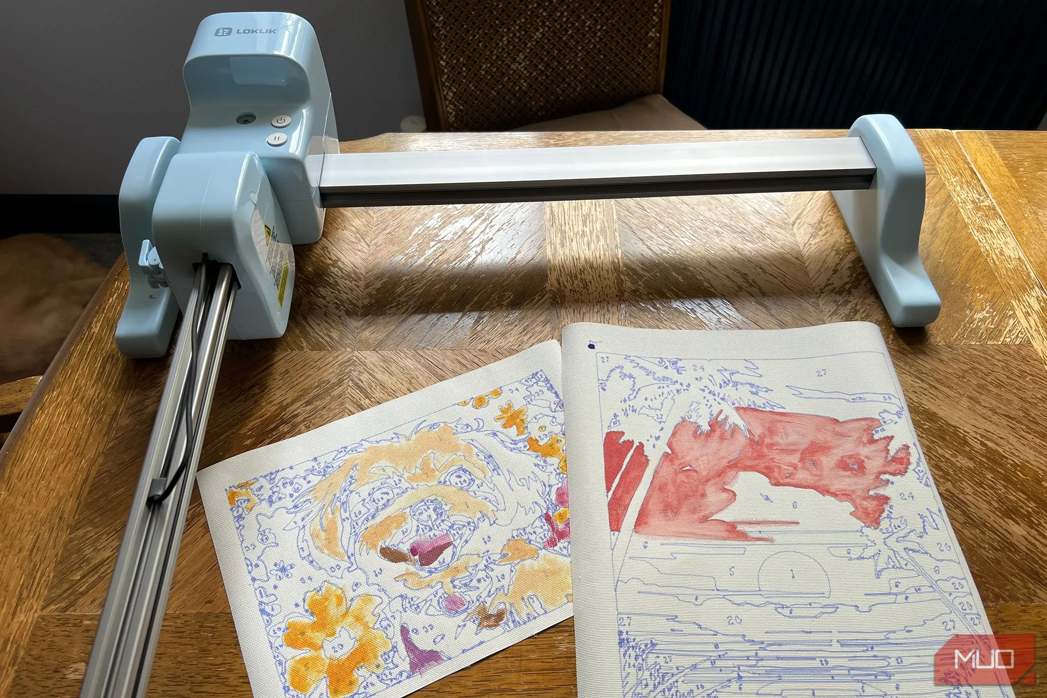 Hai bức tranh tô màu theo số đã hoàn thiện đặt cạnh máy LOKLiK iPaint, thể hiện thành quả sáng tạo.