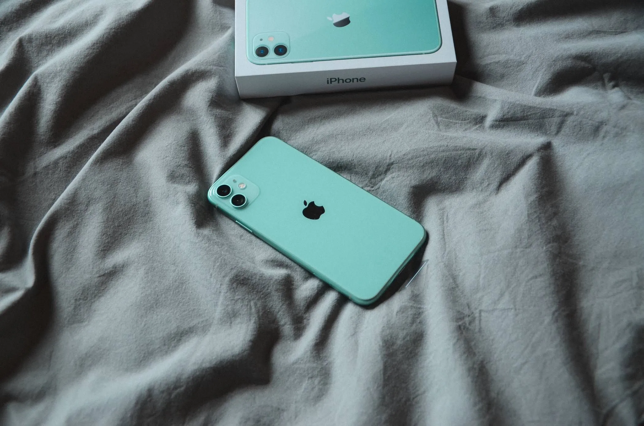 iPhone 11 màu xanh mint nằm trên chăn, thể hiện chất lượng hoàn thiện bền bỉ