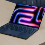 MacBook Pro M4 với màn hình nghiêng trên bàn gỗ, tượng trưng cho thế hệ Mac mới chạy Apple Silicon
