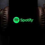 Màn hình điện thoại hiển thị ứng dụng Spotify đang phát nhạc, tai nghe được cắm vào điện thoại, minh họa khả năng điều khiển Spotify trên Google Maps khi lái xe an toàn.