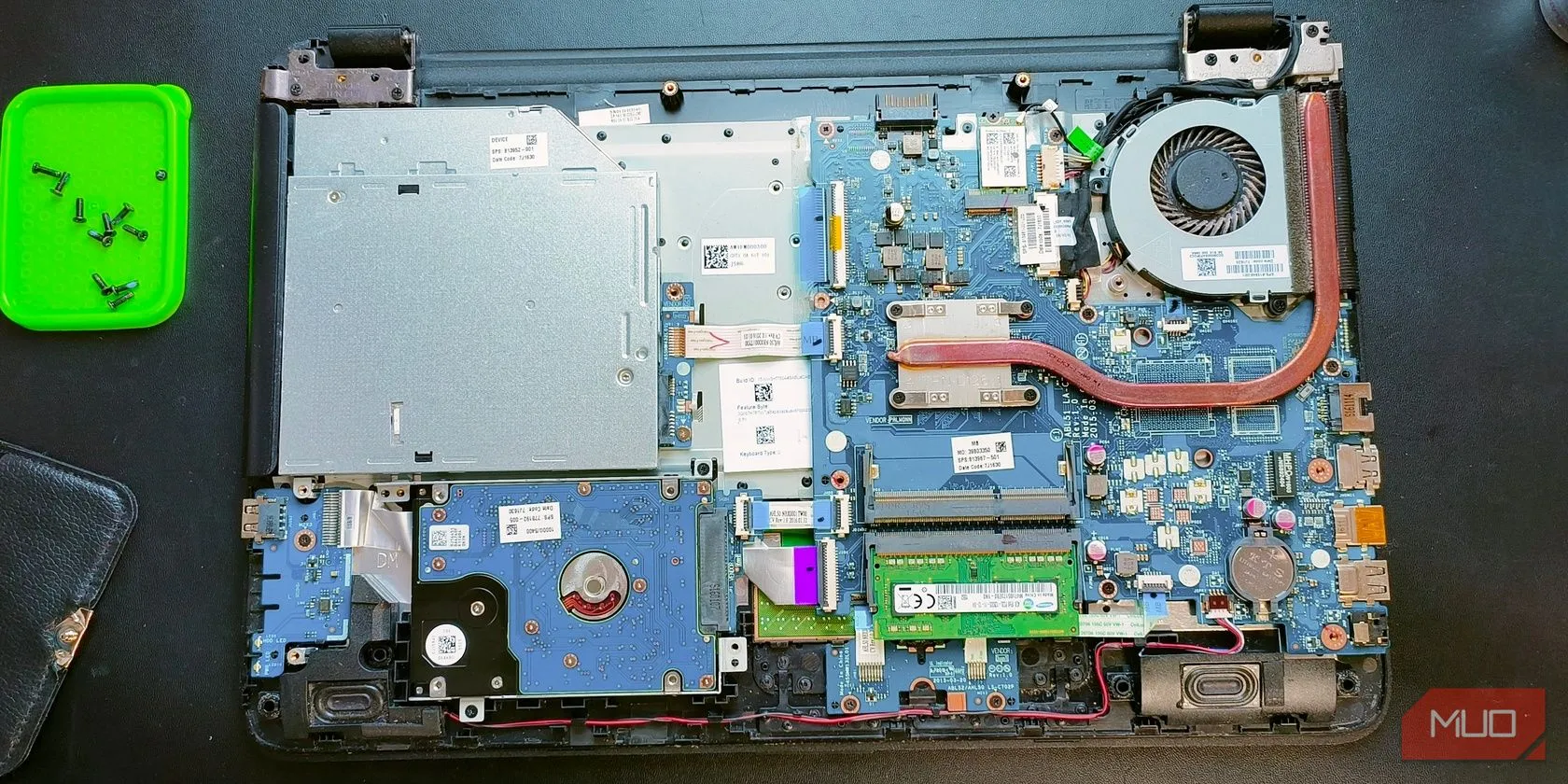 Mặt sau một chiếc laptop đang mở, để lộ các thành phần bên trong như quạt tản nhiệt và ống dẫn nhiệt, minh họa quy trình vệ sinh