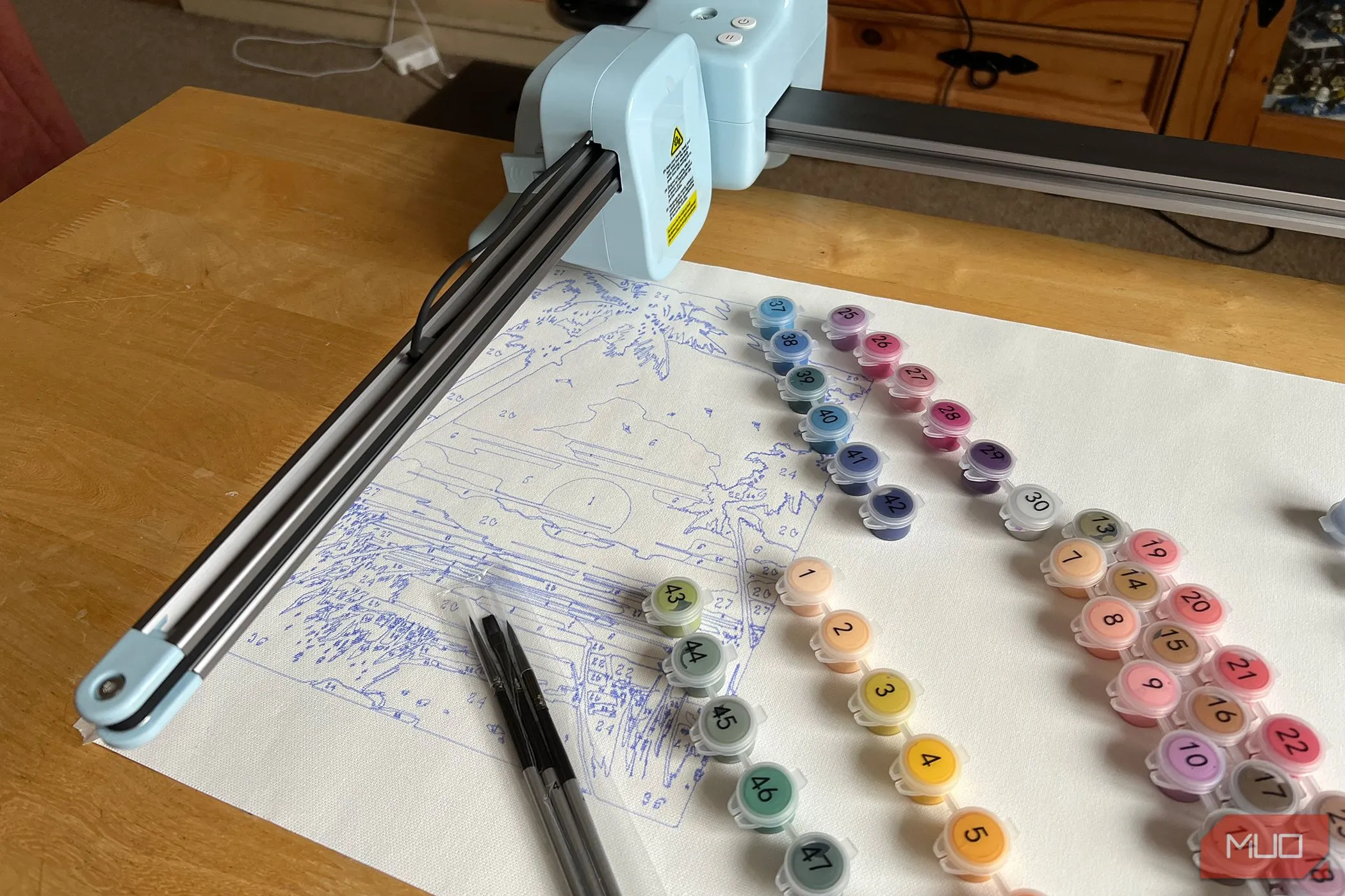 Máy LOKLiK iPaint với bức tranh hoàng hôn đang vẽ dang dở và các lọ màu được đánh số.