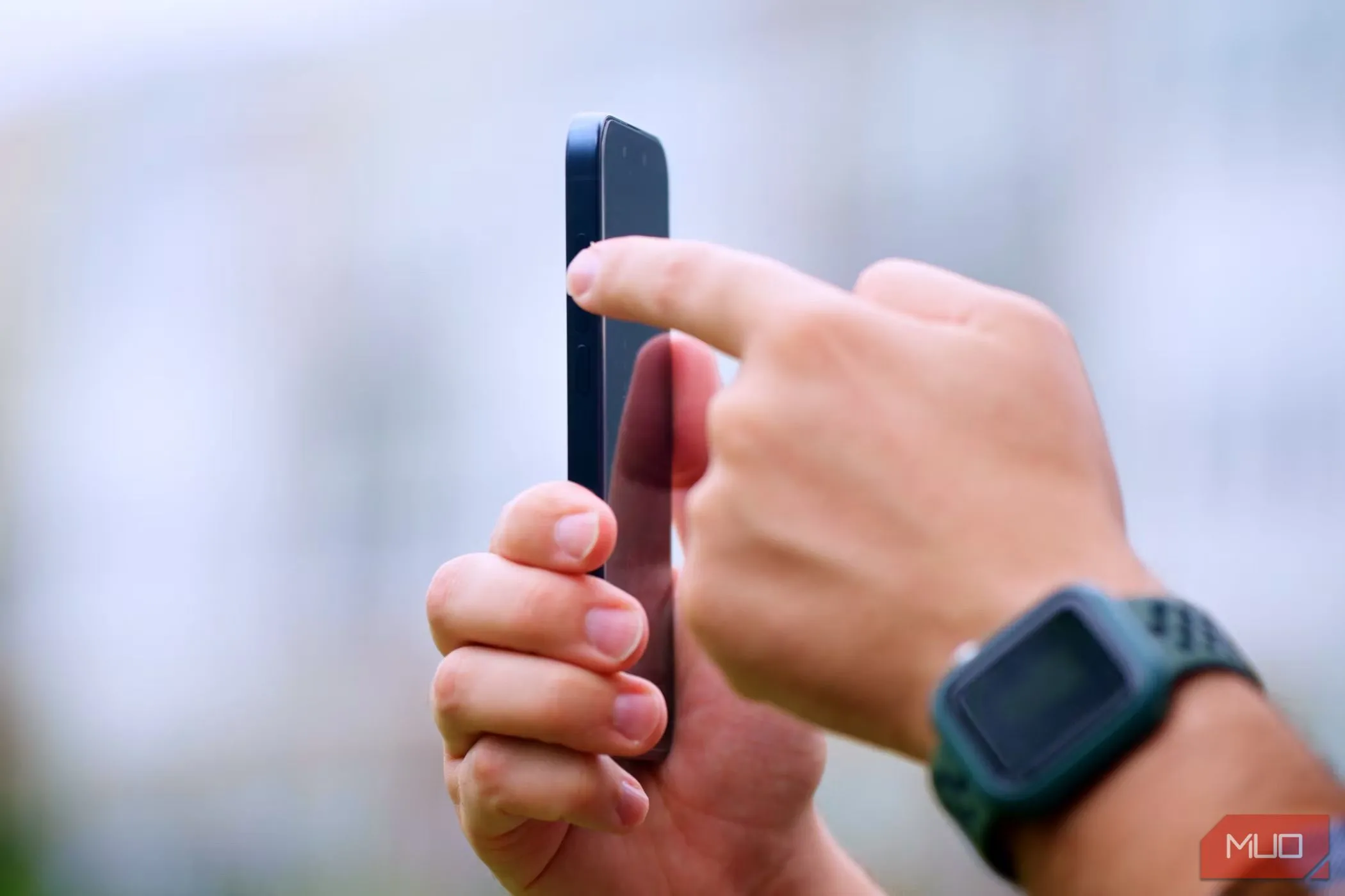 Người đàn ông đang cầm iPhone 15 Pro trong tay phải, ngón trỏ tay trái nhấn vào nút tác vụ (Action Button) ở cạnh bên