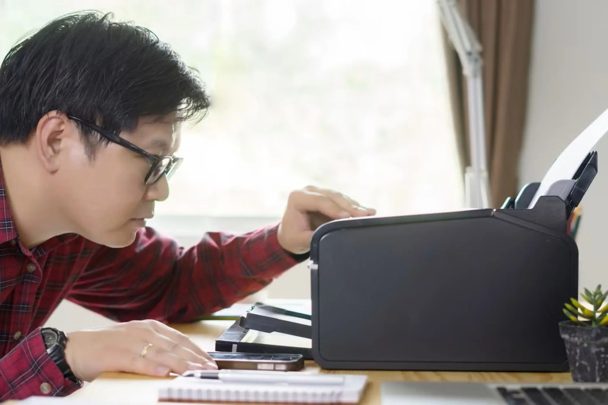 Người đàn ông đang xem xét máy in trên bàn làm việc, minh họa vấn đề tương thích và hỗ trợ hạn chế của Chromebook đối với một số thiết bị ngoại vi chuyên dụng.