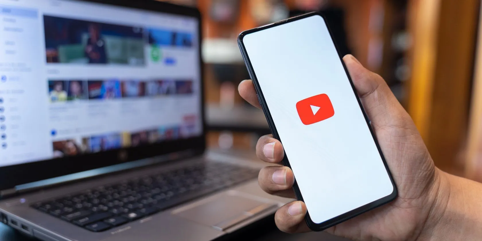 Người dùng cầm điện thoại với ứng dụng YouTube và trang web YouTube phía sau, minh họa việc nhận diện lừa đảo