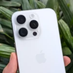 Người dùng cầm iPhone 16 Pro màu trắng trước khóm cây xanh, thể hiện thiết kế sang trọng