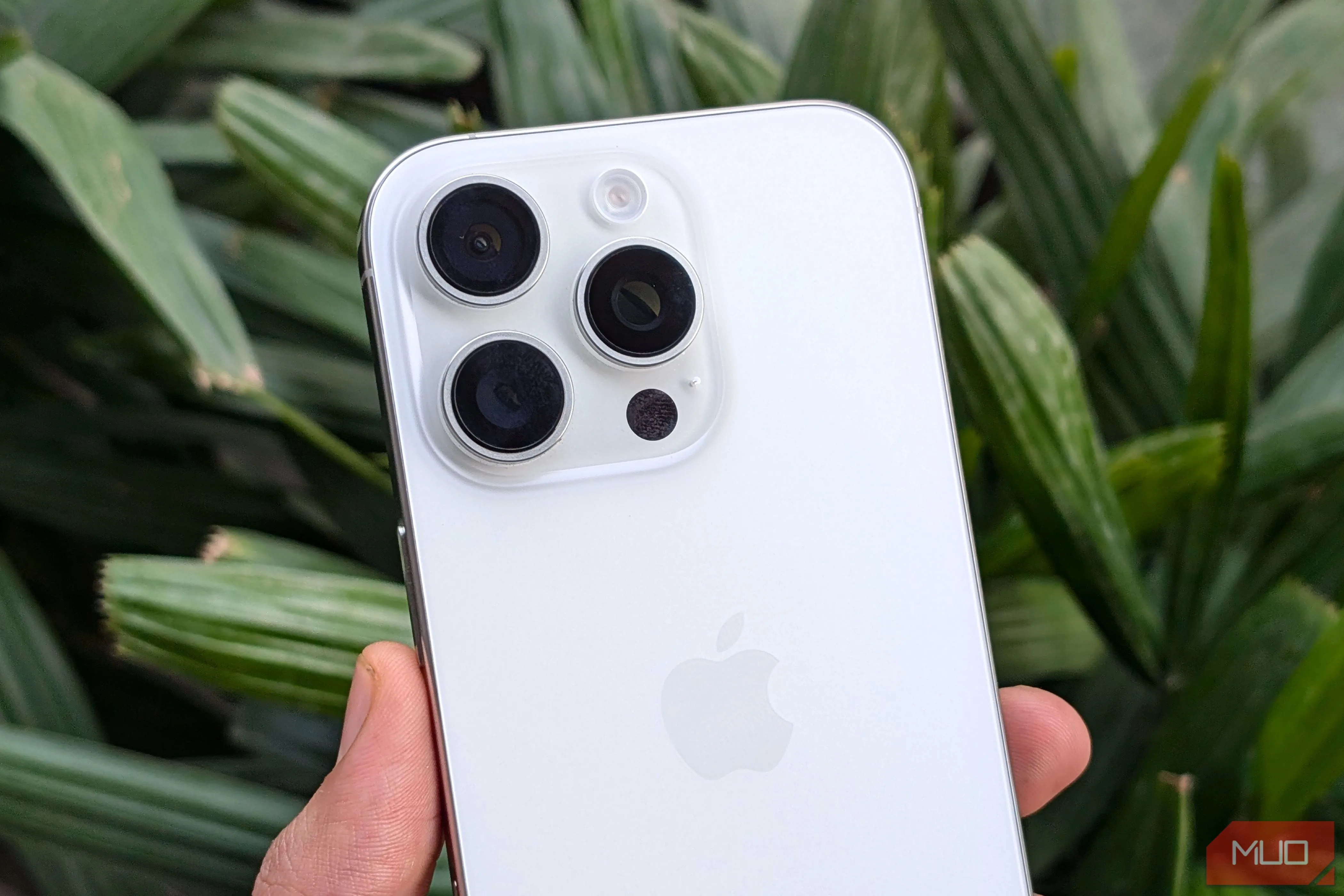 Người dùng cầm iPhone 16 Pro màu trắng trước khóm cây xanh, thể hiện thiết kế sang trọng