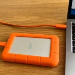 Ổ cứng ngoài di động màu đen được cắm vào cổng USB của một chiếc máy tính xách tay màu bạc, minh họa cách sao lưu dữ liệu trực tiếp.
