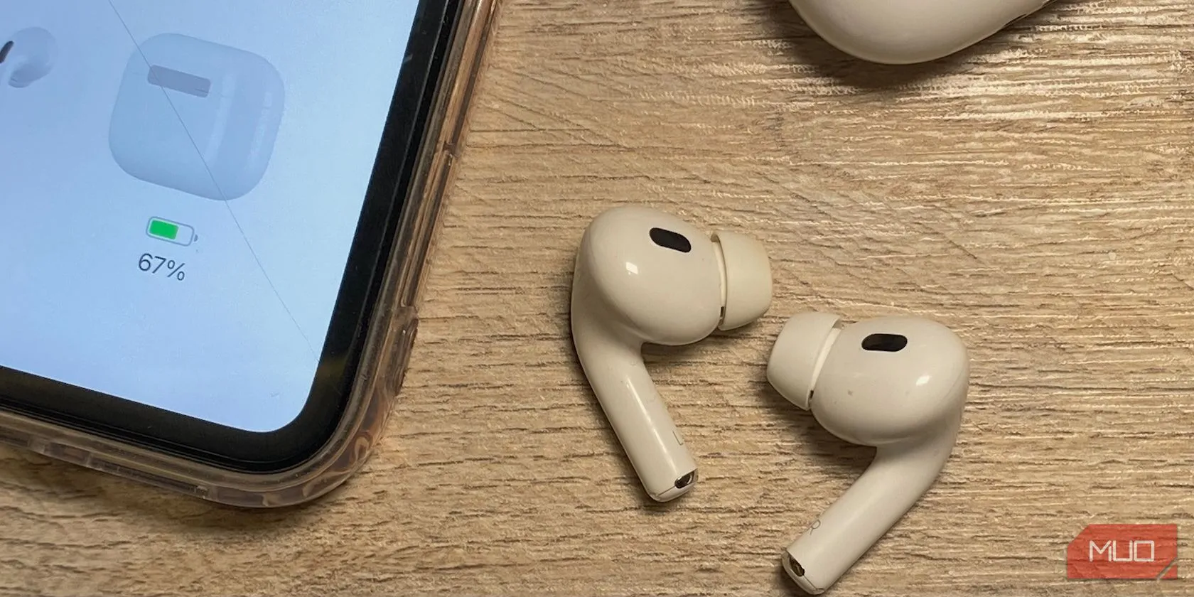 Tai nghe AirPods (thế hệ thường) đặt cạnh iPhone trên bàn gỗ, minh họa sự khác biệt về chiều dài thân tai nghe giữa các thế hệ