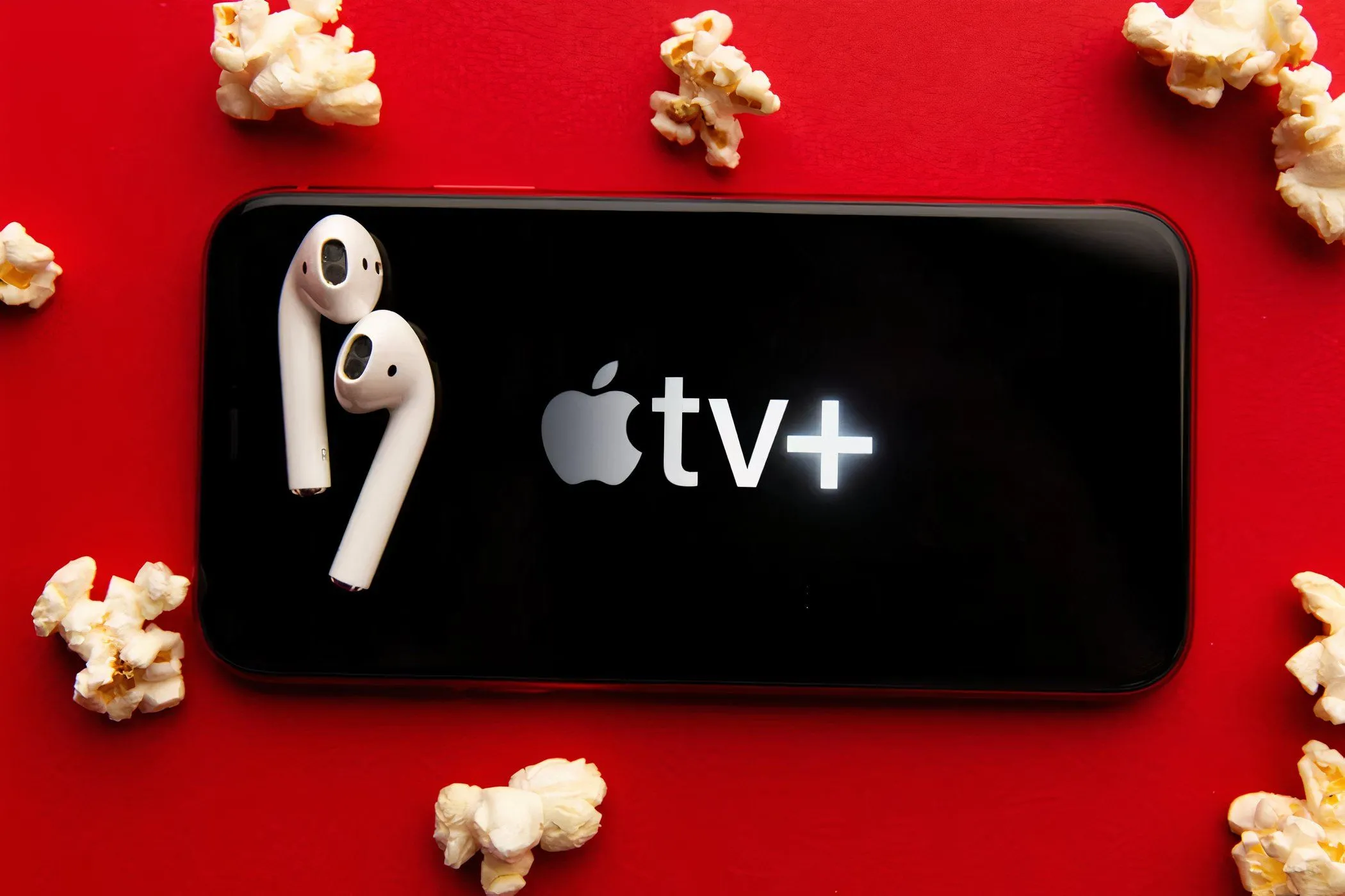 Ứng dụng Apple TV+ hiển thị trên màn hình điện thoại di động, đi kèm với bắp rang bơ và tai nghe, gợi mở trải nghiệm xem phim giải trí tại nhà.