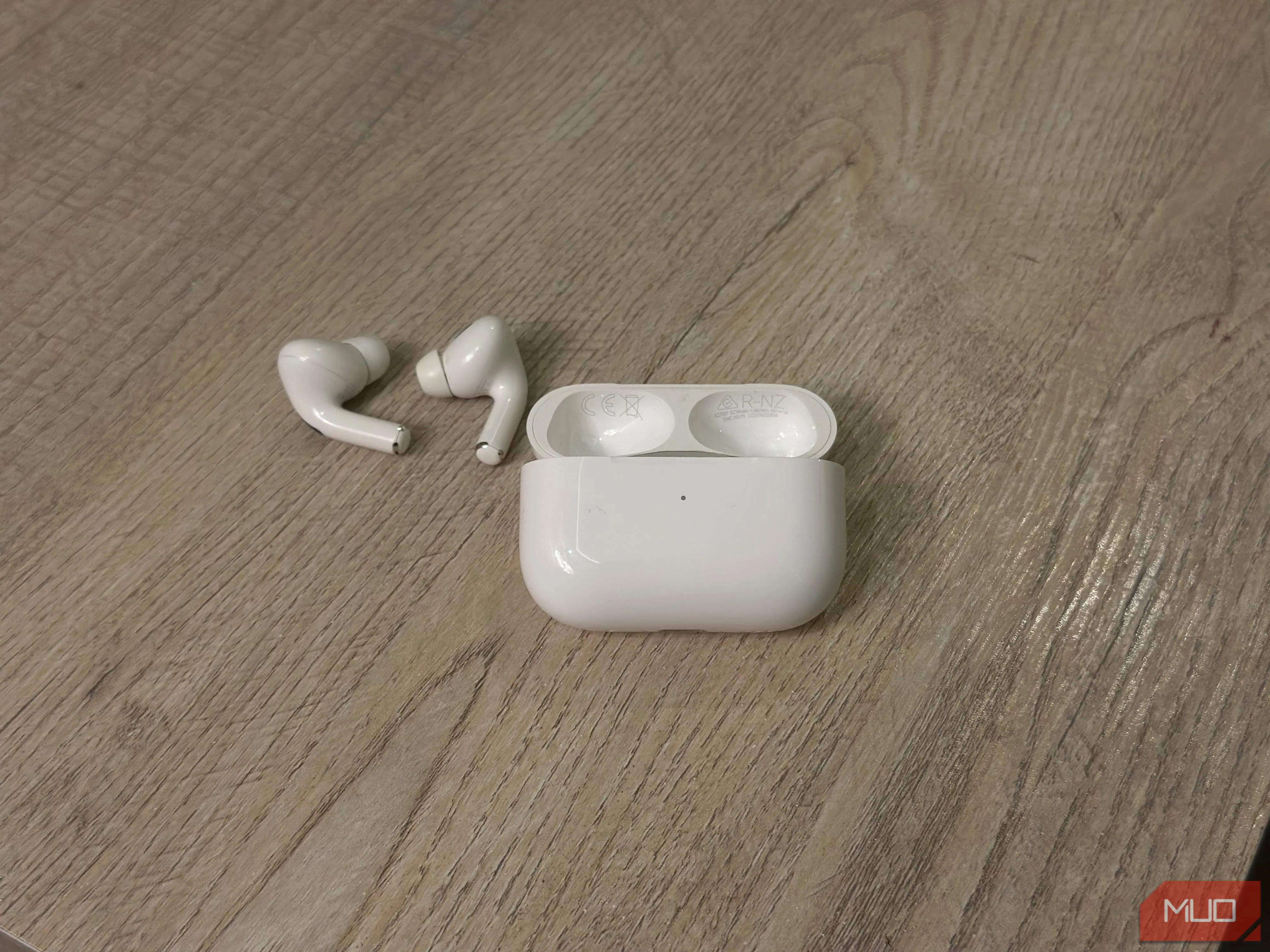 Vỏ sạc AirPods và tai nghe đặt trên bàn, minh họa vị trí tìm số model và số serial bên trong nắp
